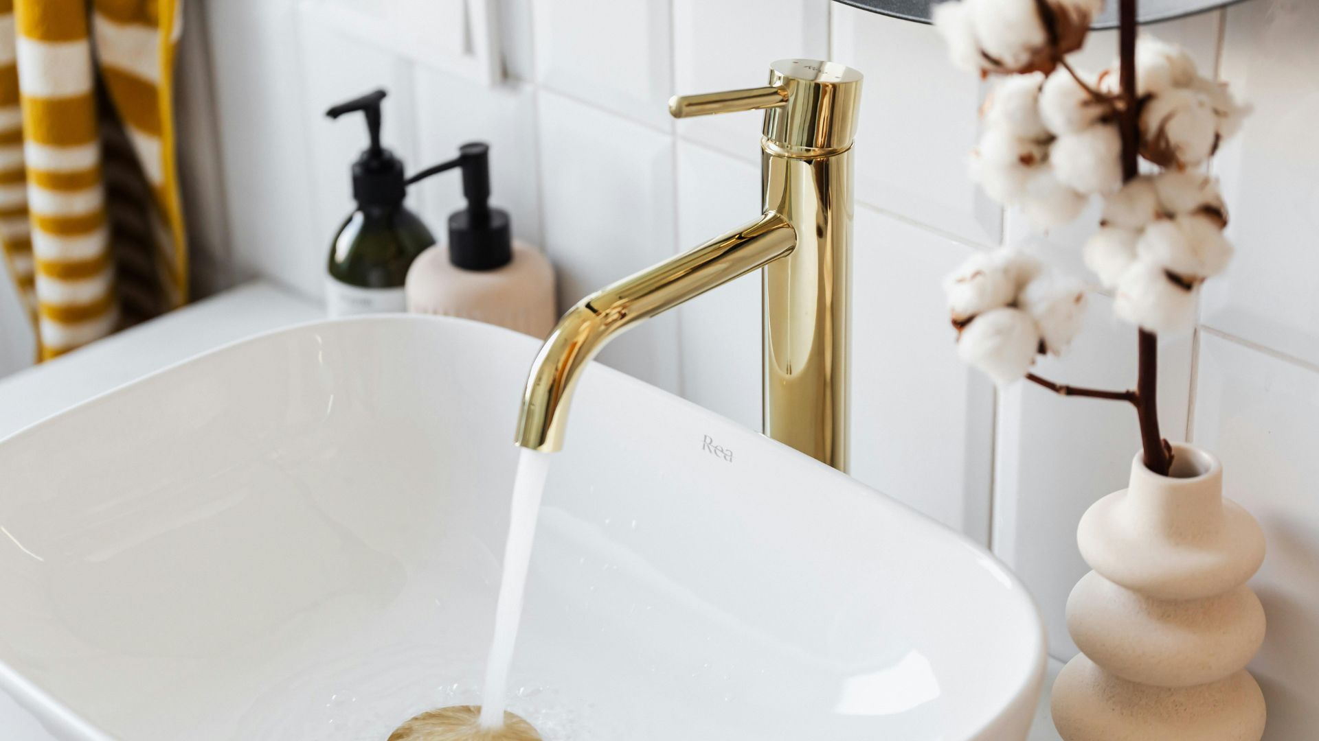 Gold faucet pouring water into white sink with cotton branch in background