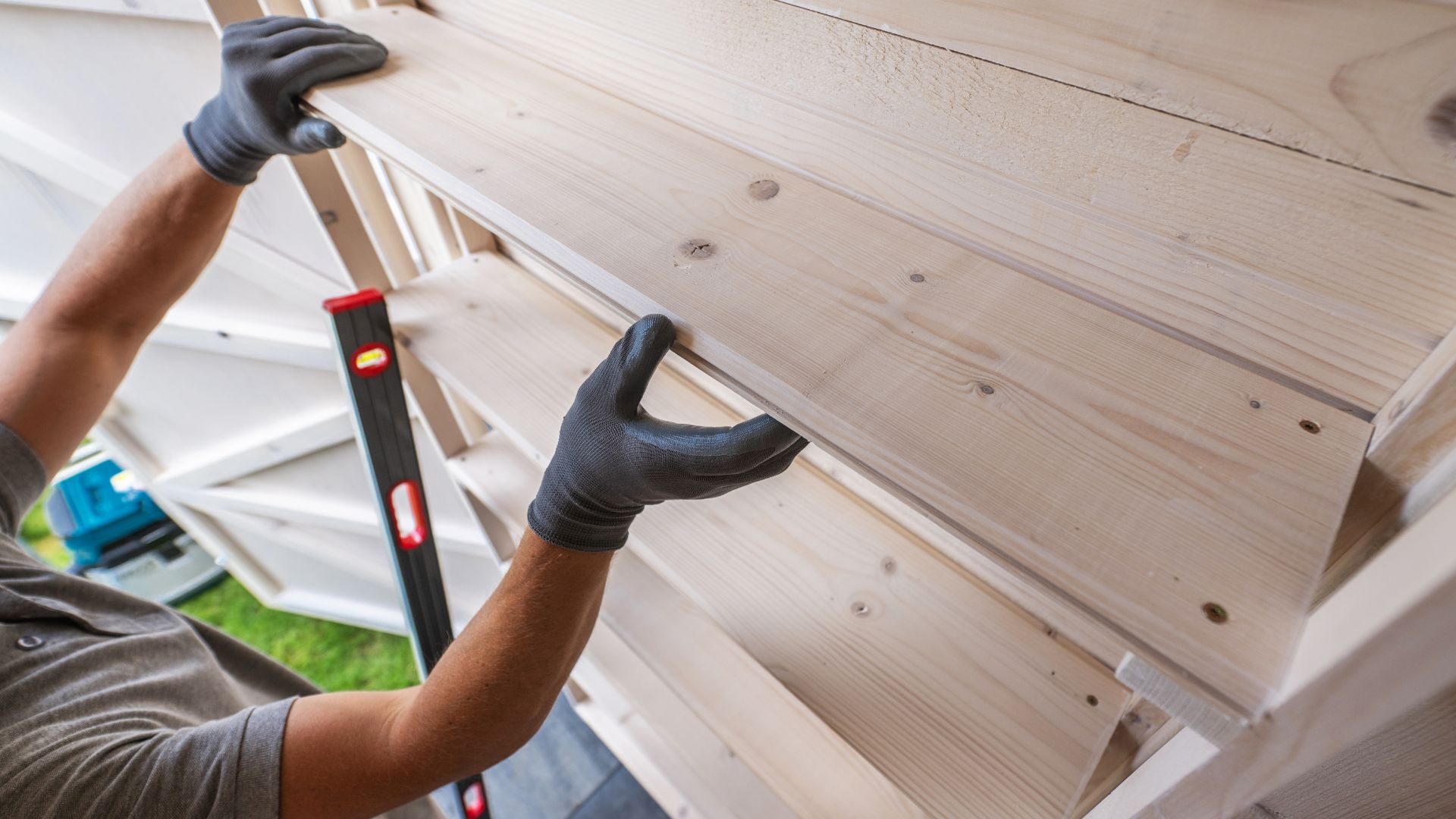 Worker installing wooden boards using level and gloved hands