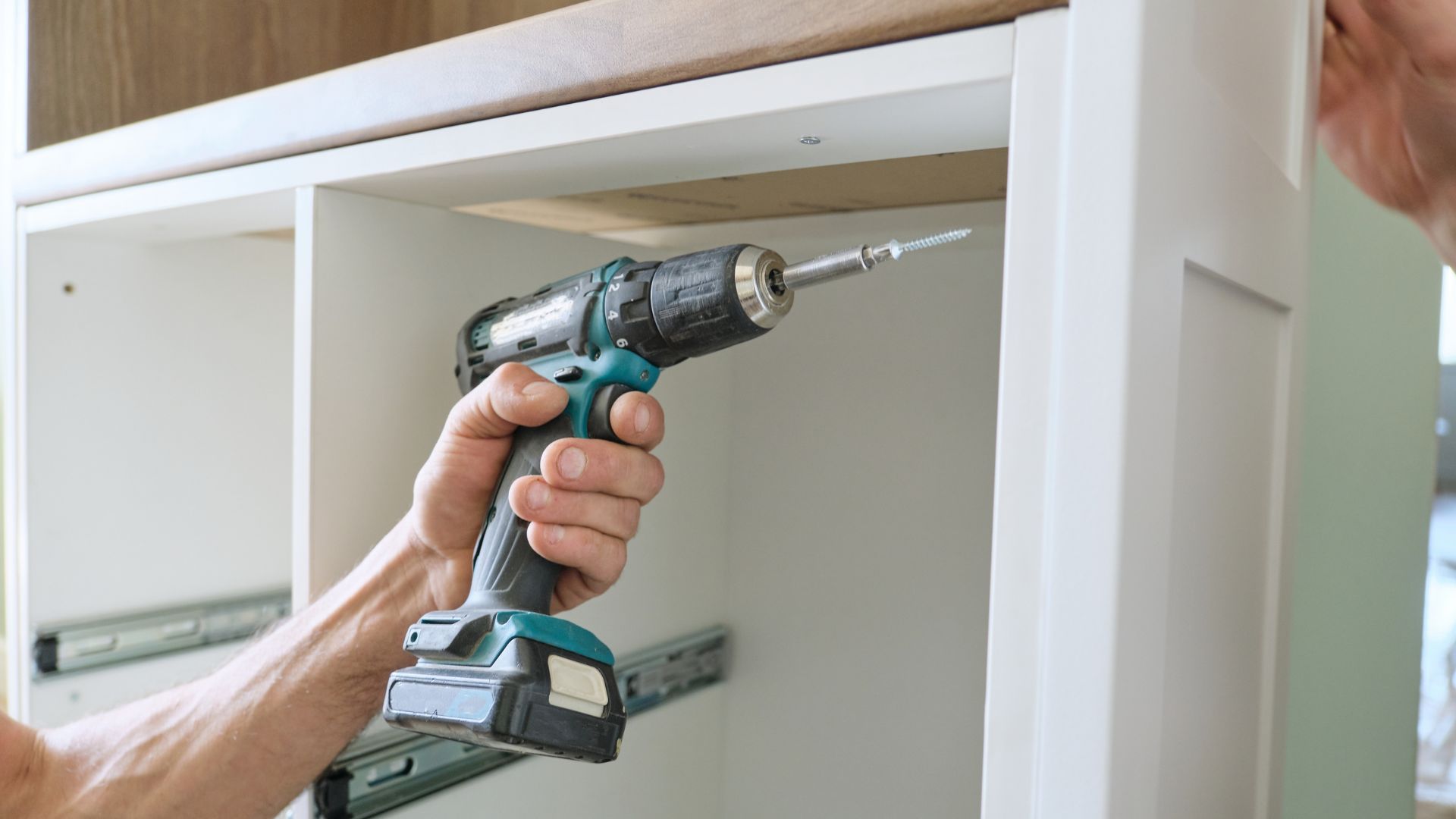 Cordless drill being used to screw into white cabinet drawer