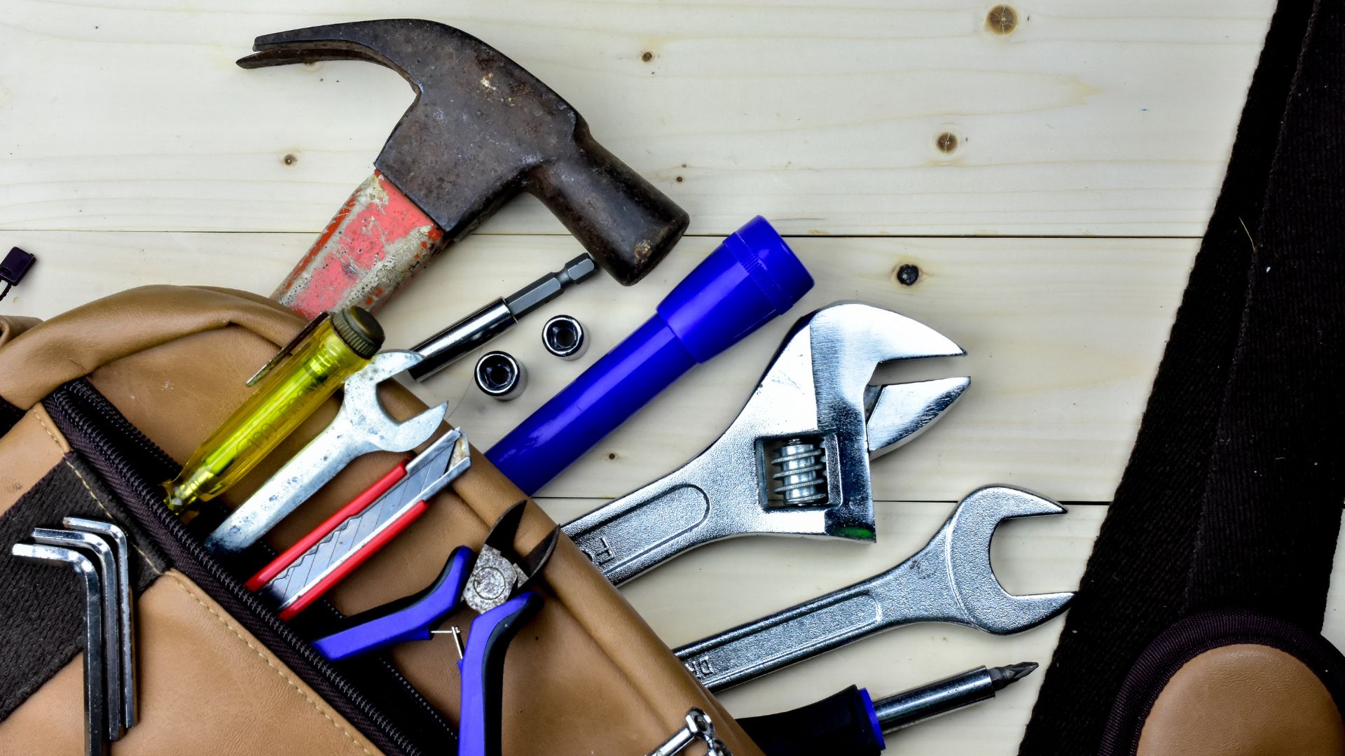 Assorted hand tools and hammer in a leather tool belt on wooden background