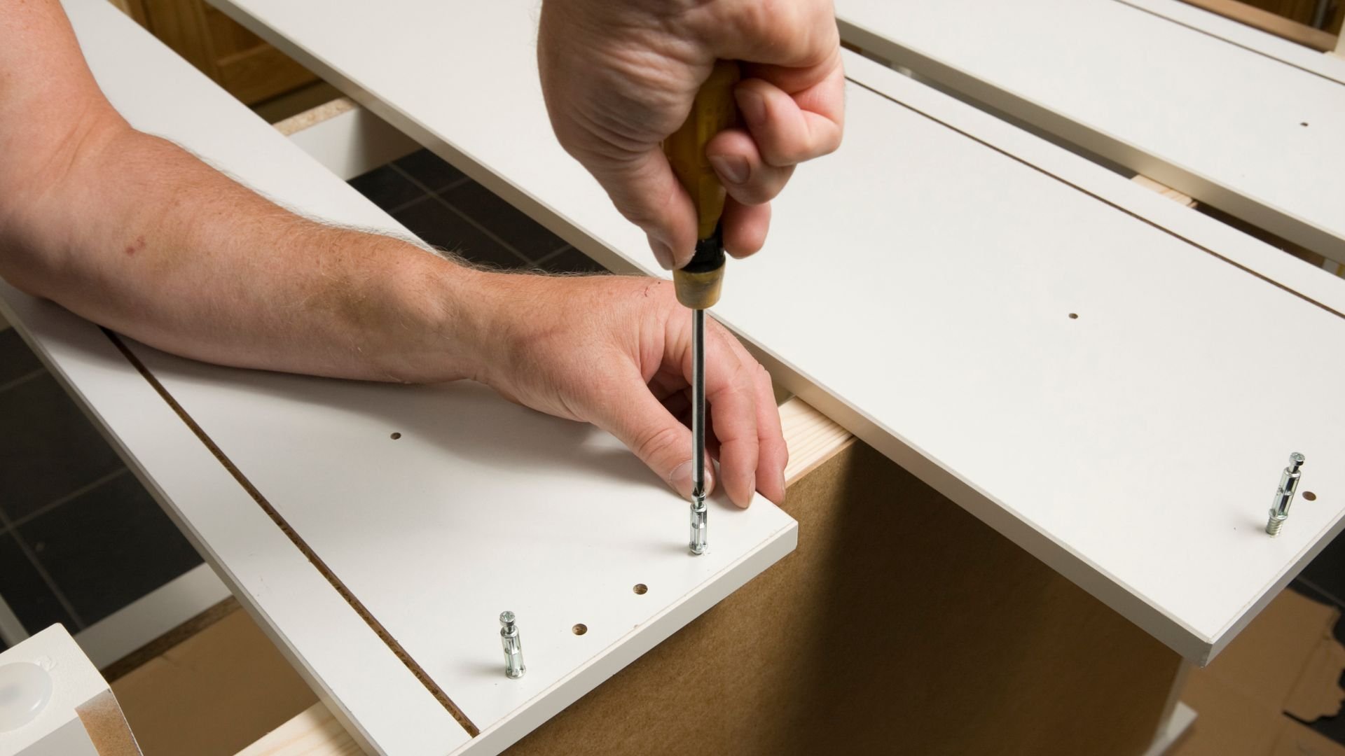Hand using screwdriver to assemble white wooden furniture or cabinet