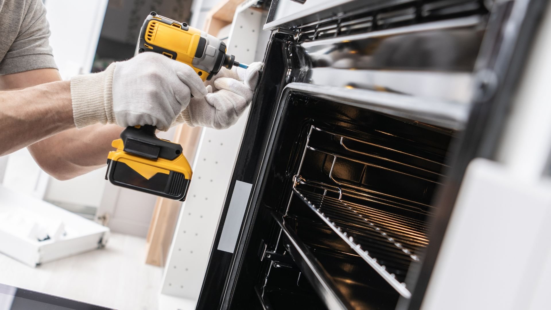 Technician repairing oven with yellow cordless drill and white gloves