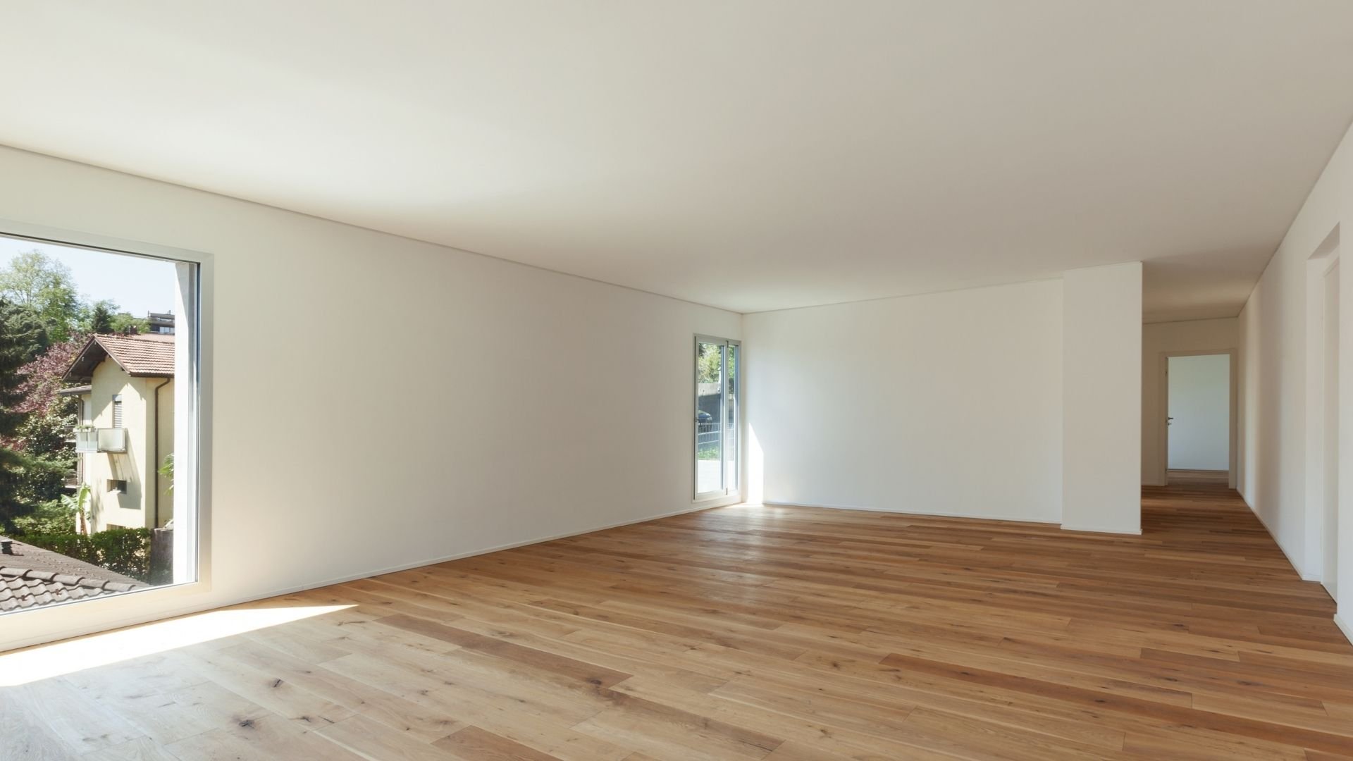 Empty room with wooden floor, white walls, and large windows