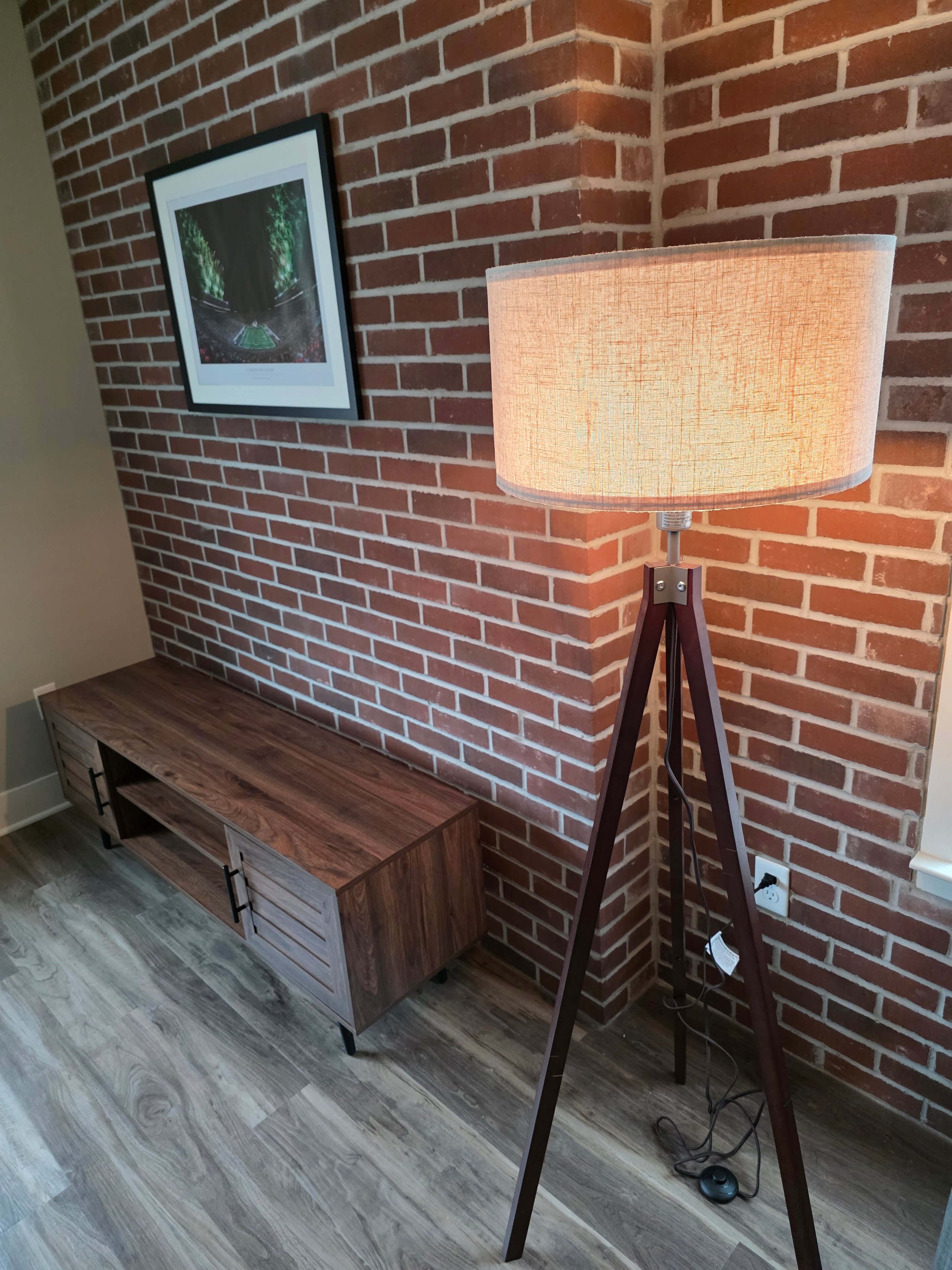 Tripod lamp next to wooden console on brick wall with framed artwork
