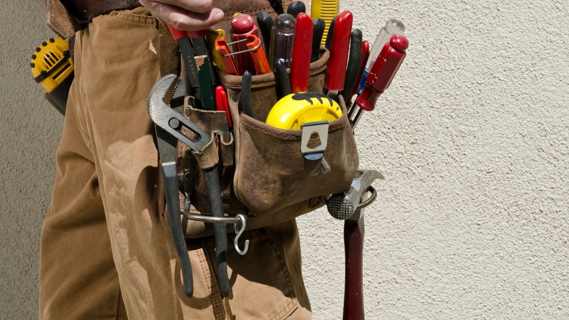 Leather tool belt filled with colorful screwdrivers, wrench, and yellow hard hat
