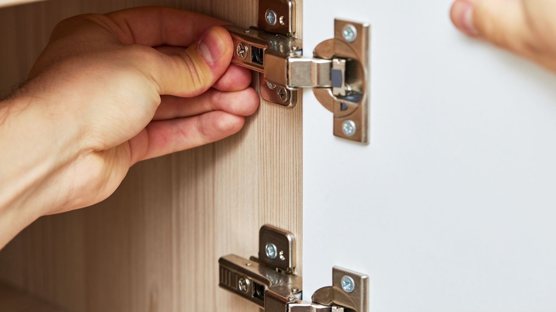 Hand adjusting metal cabinet door hinge on wooden surface