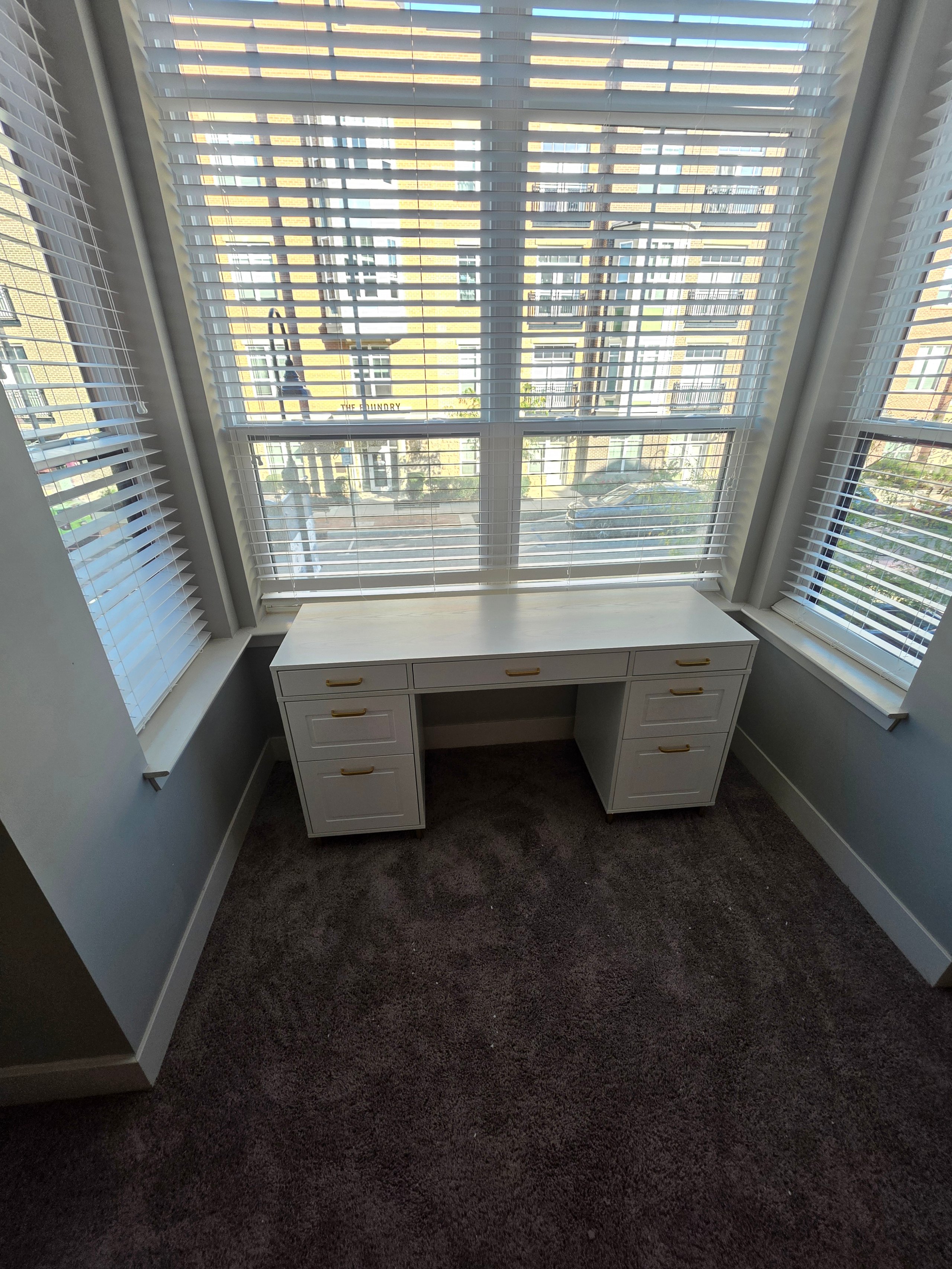 White desk near bay window with venetian blinds overlooking urban street