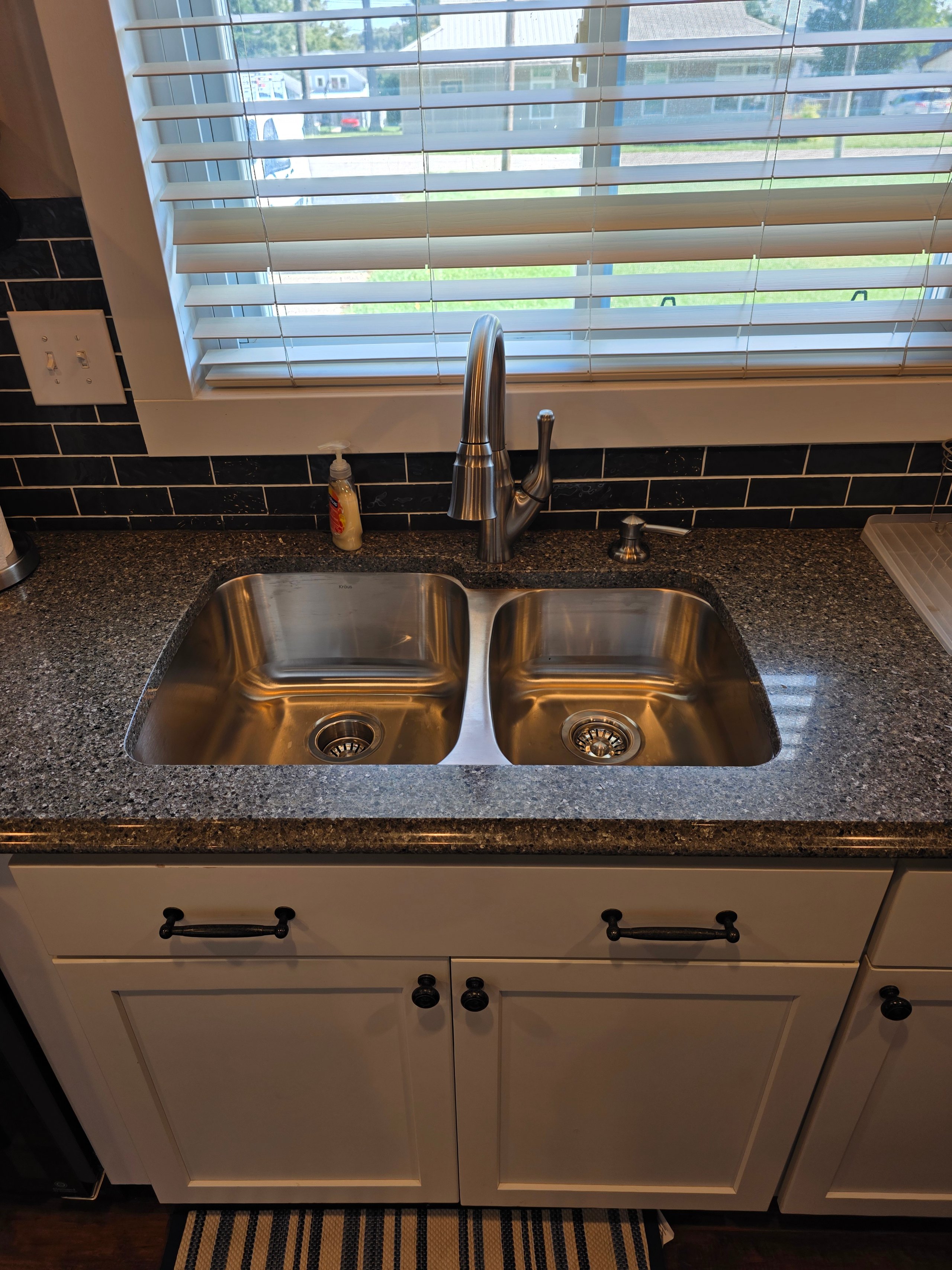 Modern kitchen sink with double basin, granite countertop, and window blinds