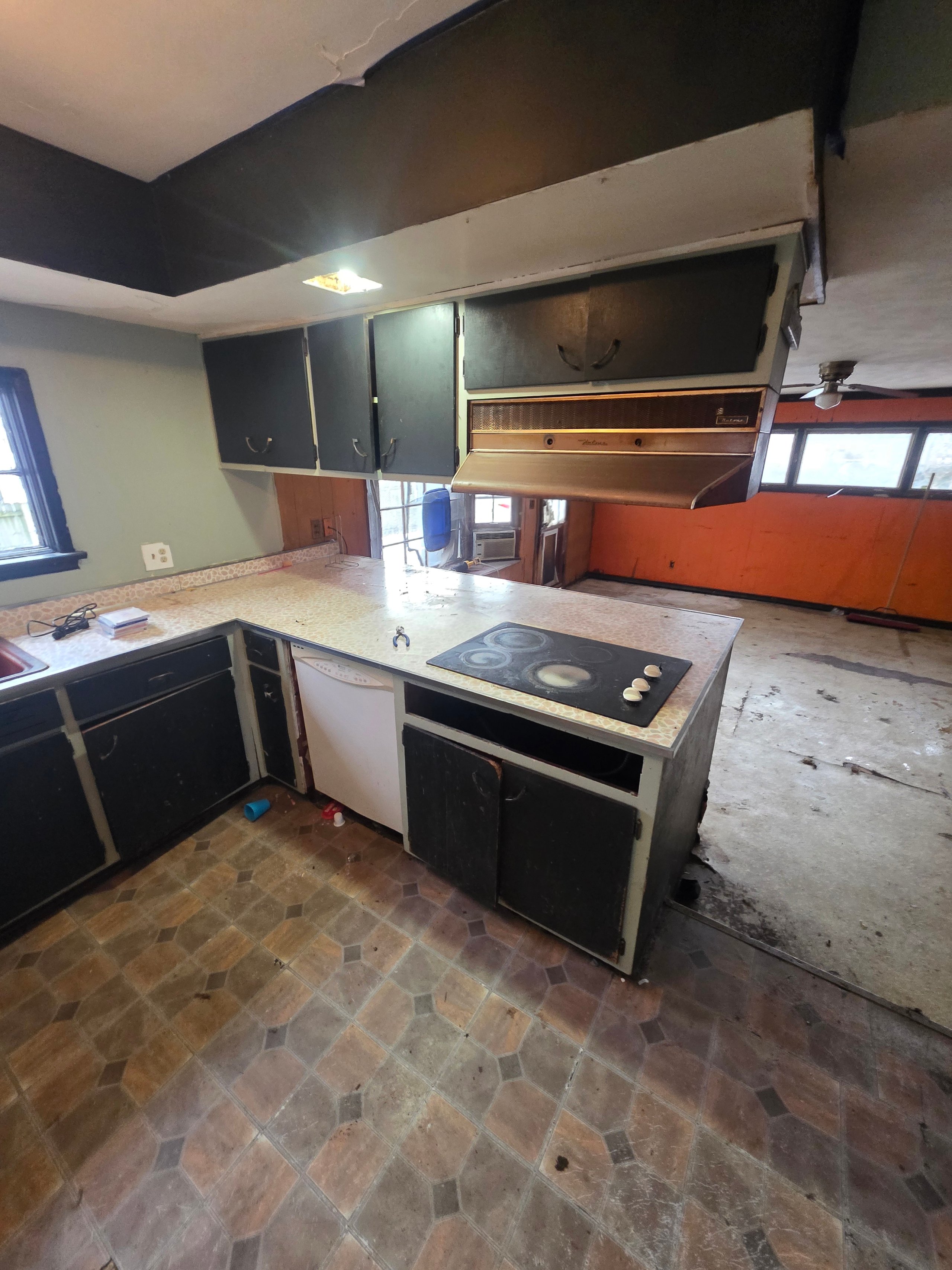 Old, worn kitchen with black cabinets, stove, and dated stone floor tiles