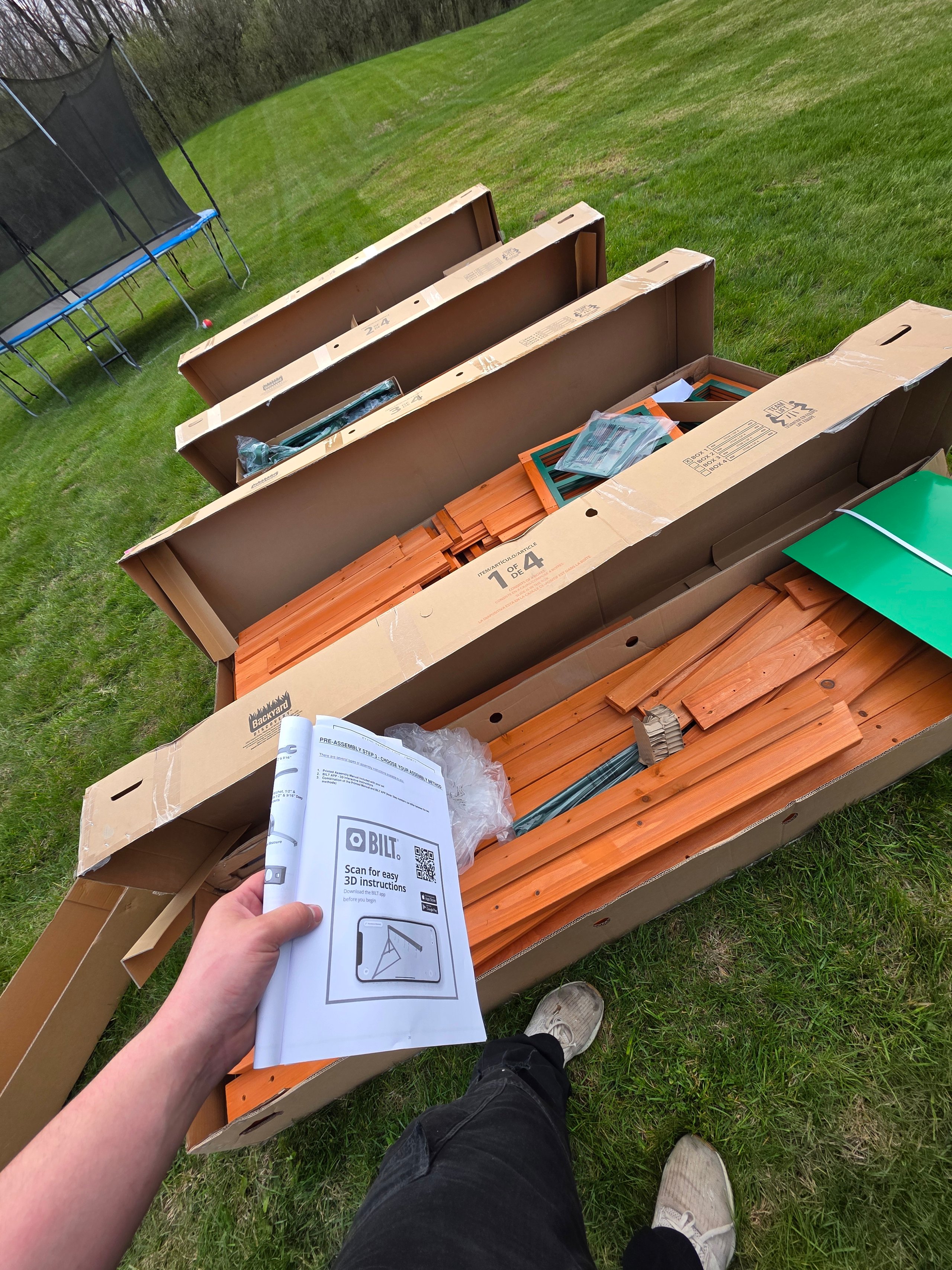 Wooden furniture kit with assembly instructions on grassy backyard with trampoline