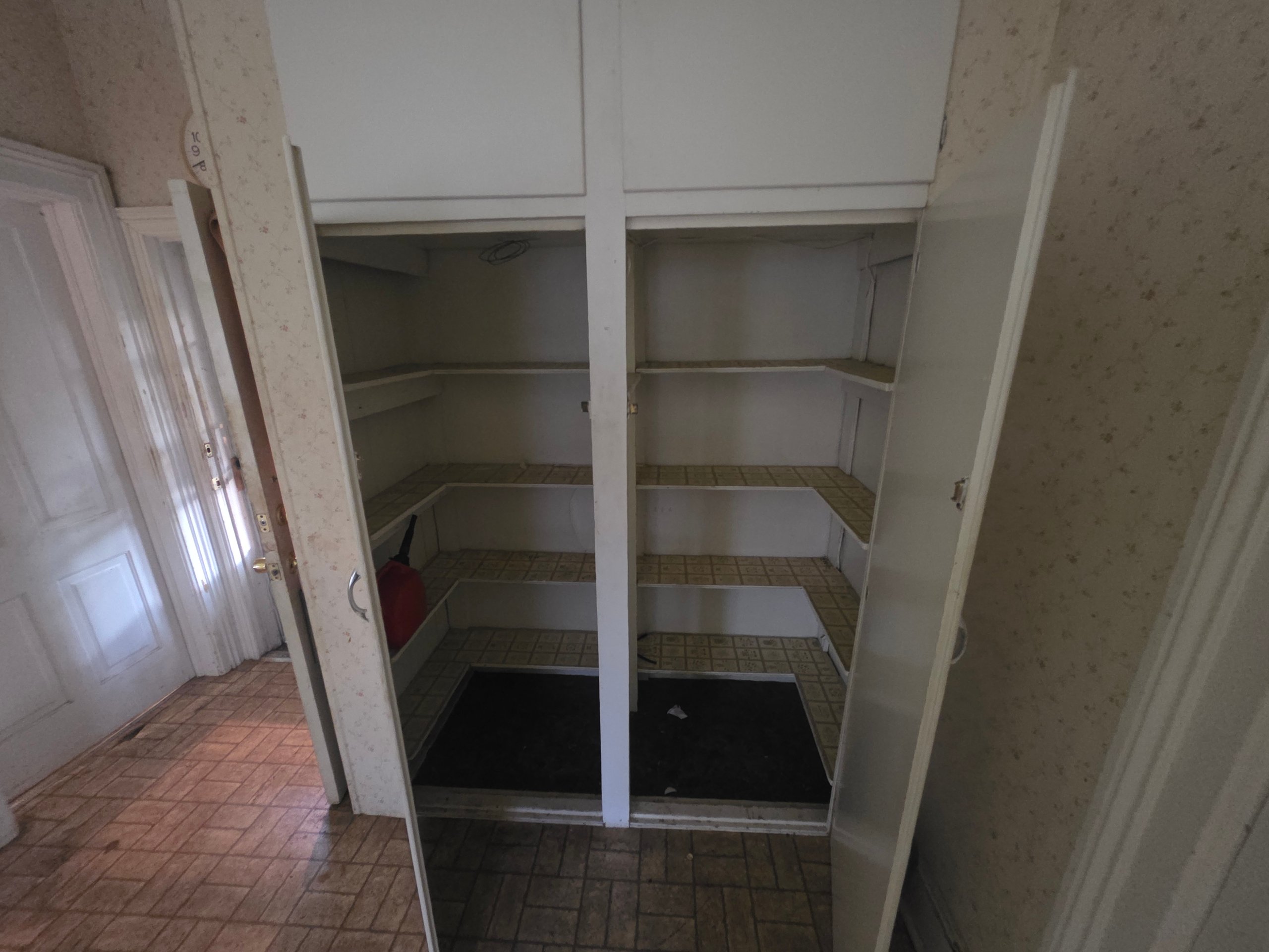 Empty white shelved closet with tiled floor and open doors