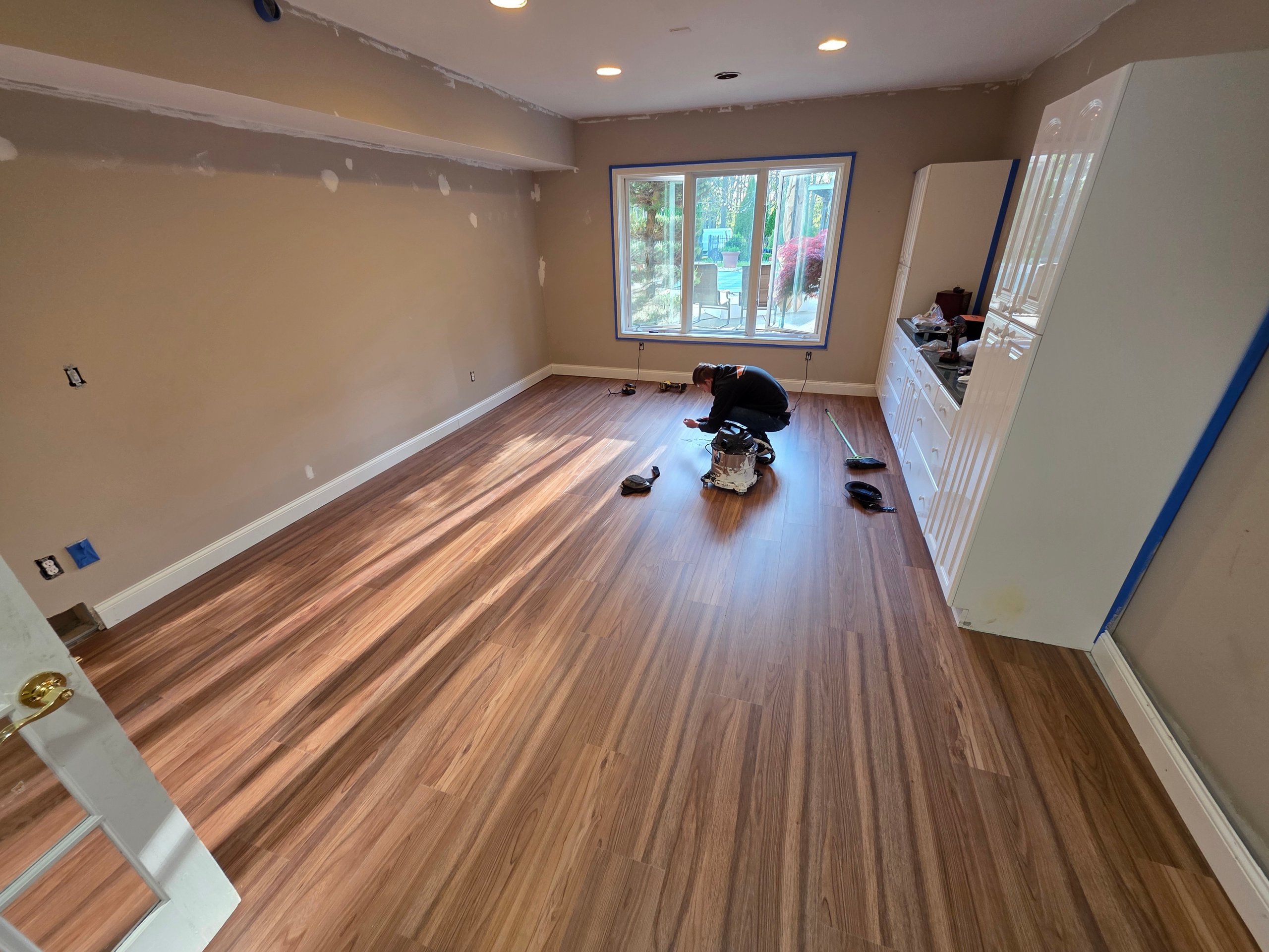Worker installing hardwood flooring in room with large window