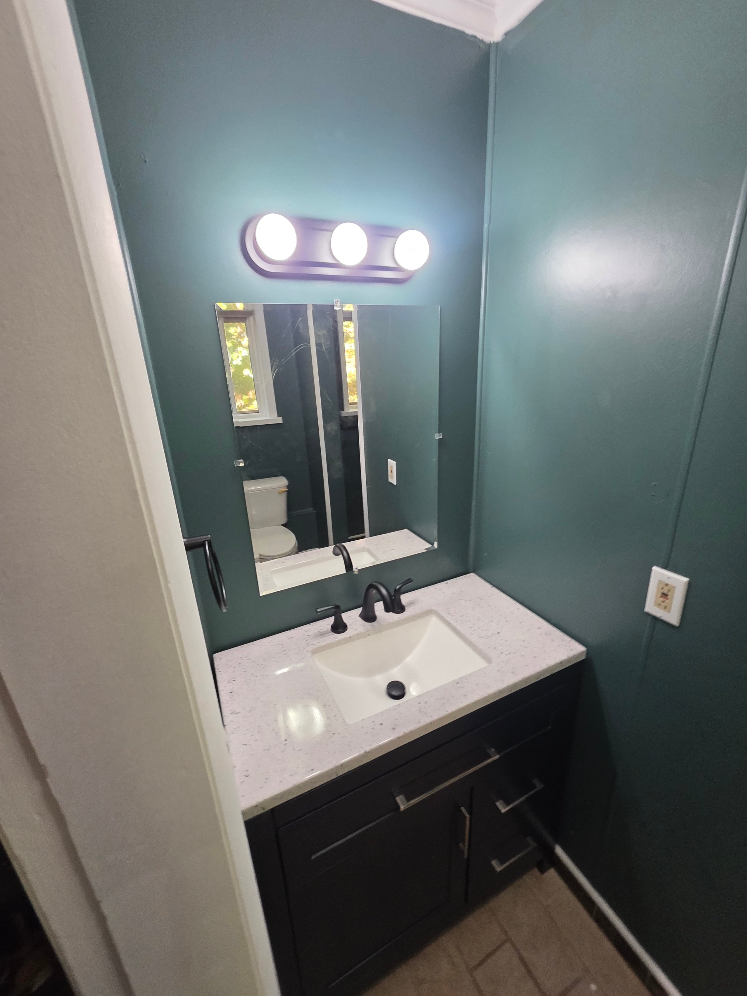 Small bathroom with teal walls, white countertop, and vanity lighting