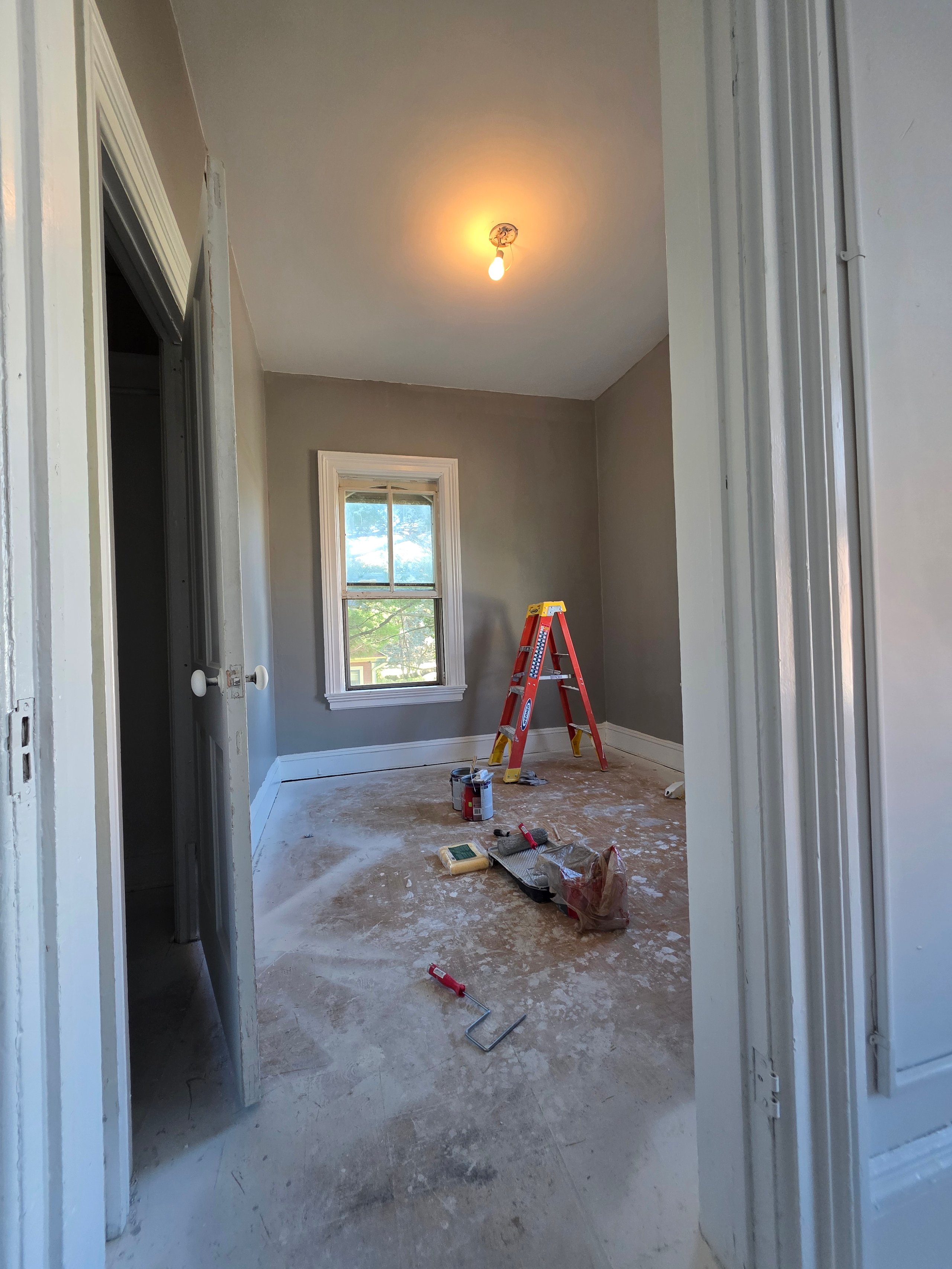 Room under renovation with ladder, paint supplies, and warm ceiling light