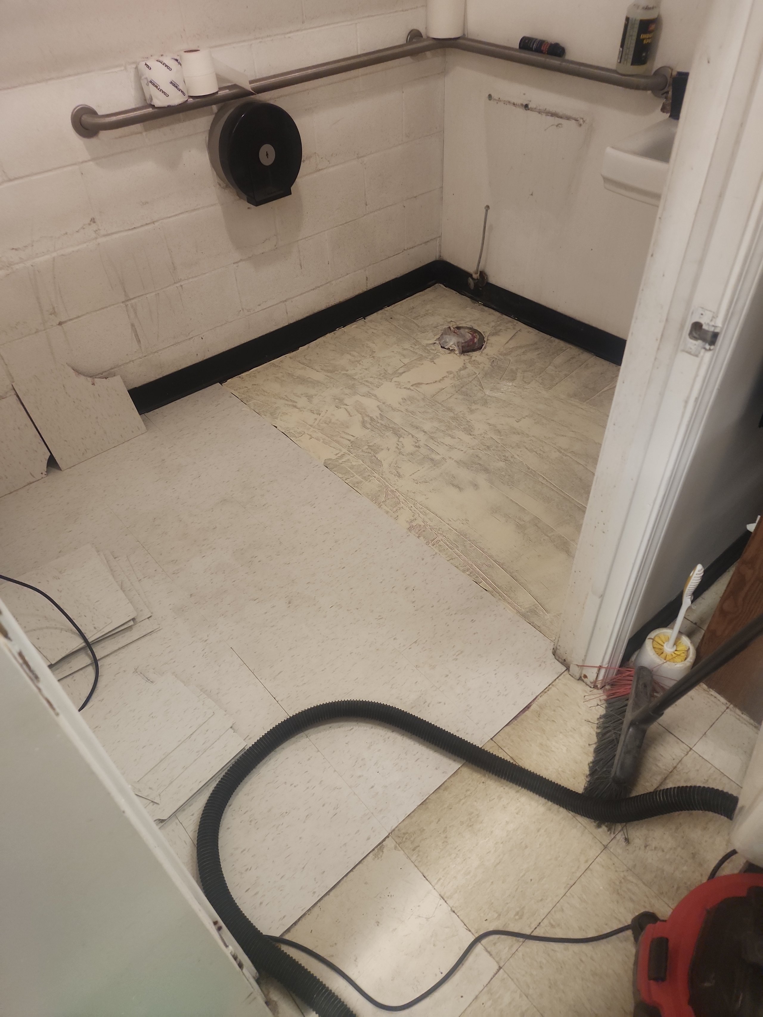 Bathroom floor with vacuum hose, toilet paper roll, and cleaning tools