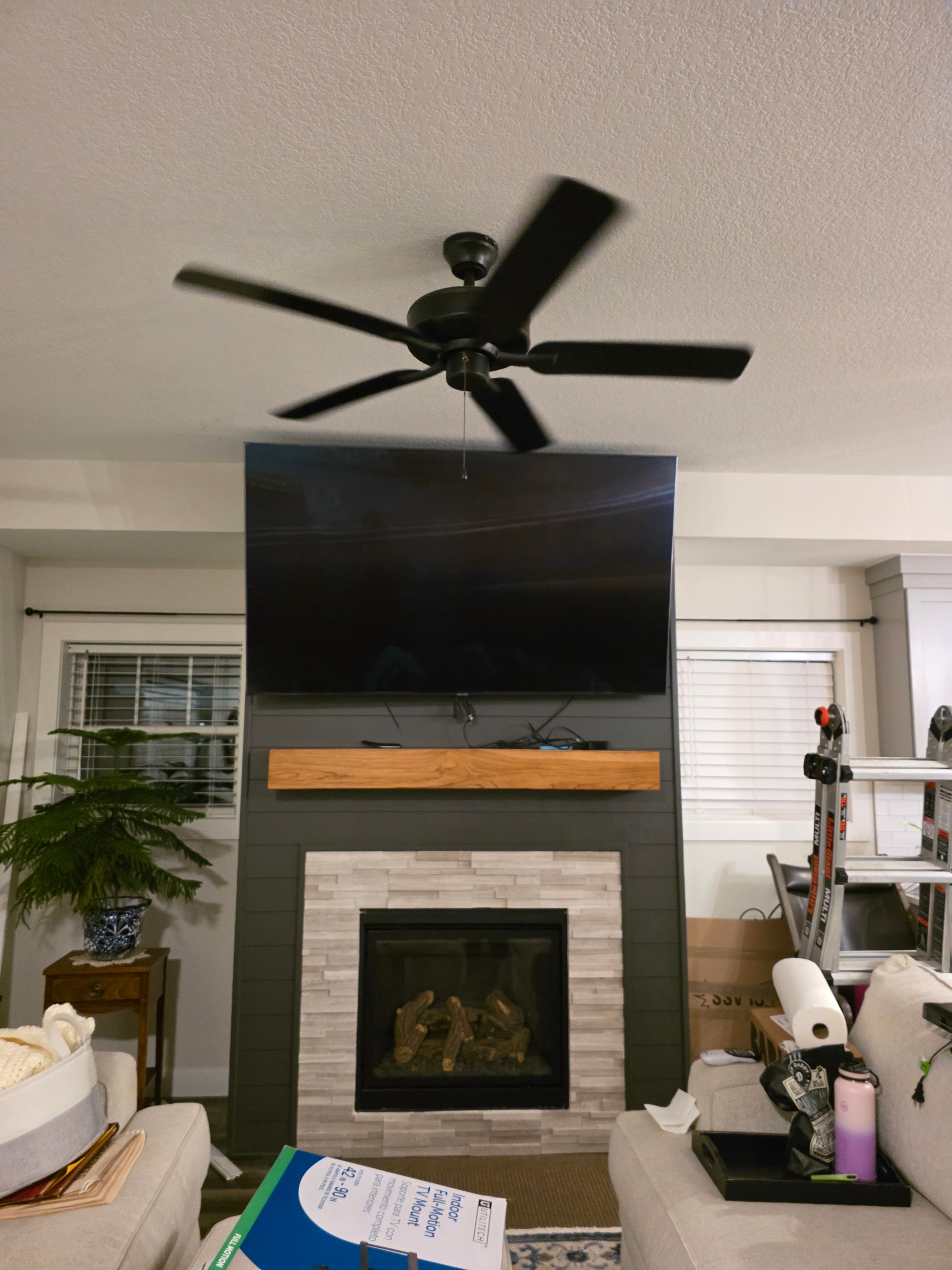 Modern living room with fireplace, TV, ceiling fan, and potted plant