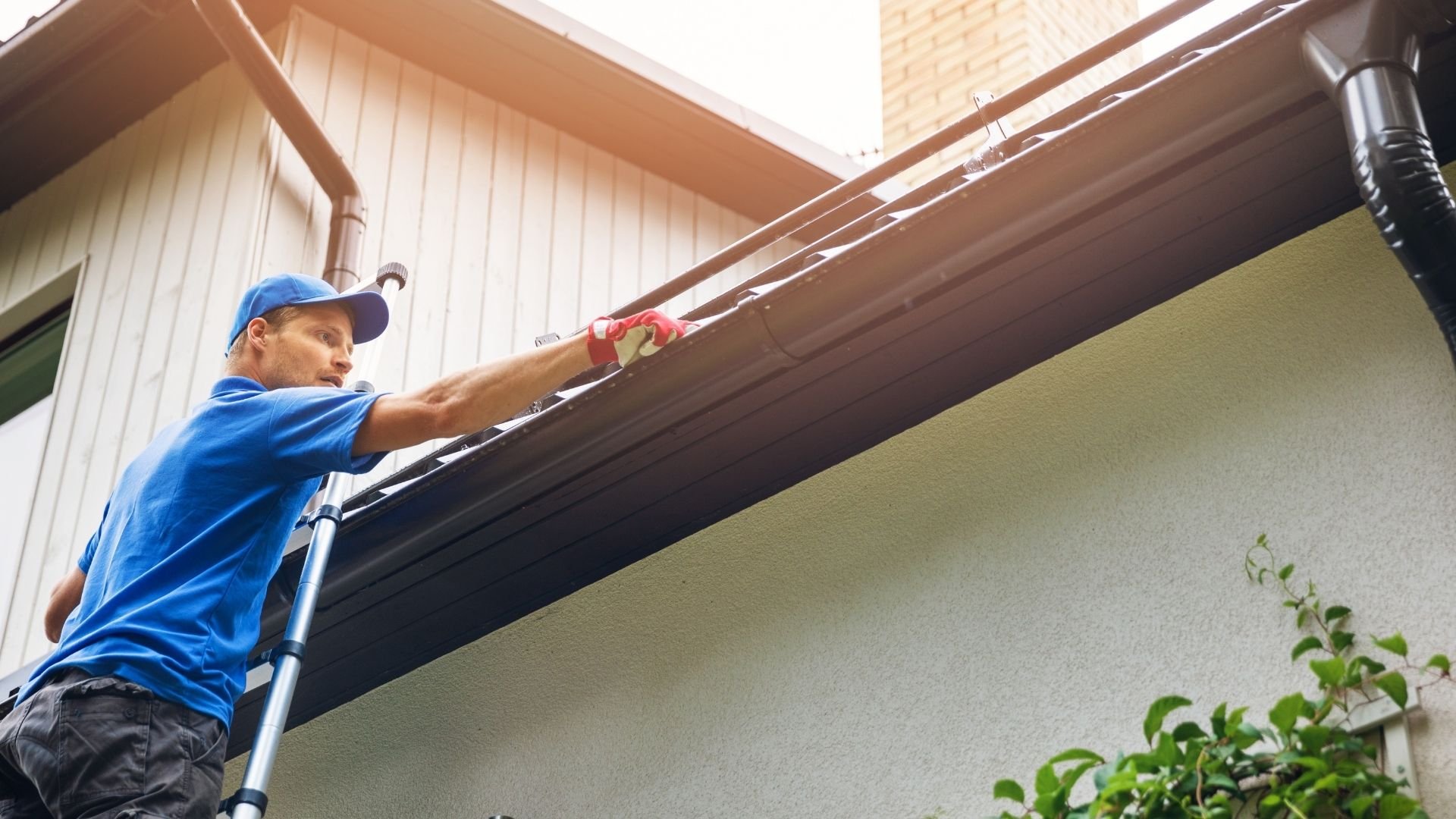 Worker on ladder cleaning gutters of residential house