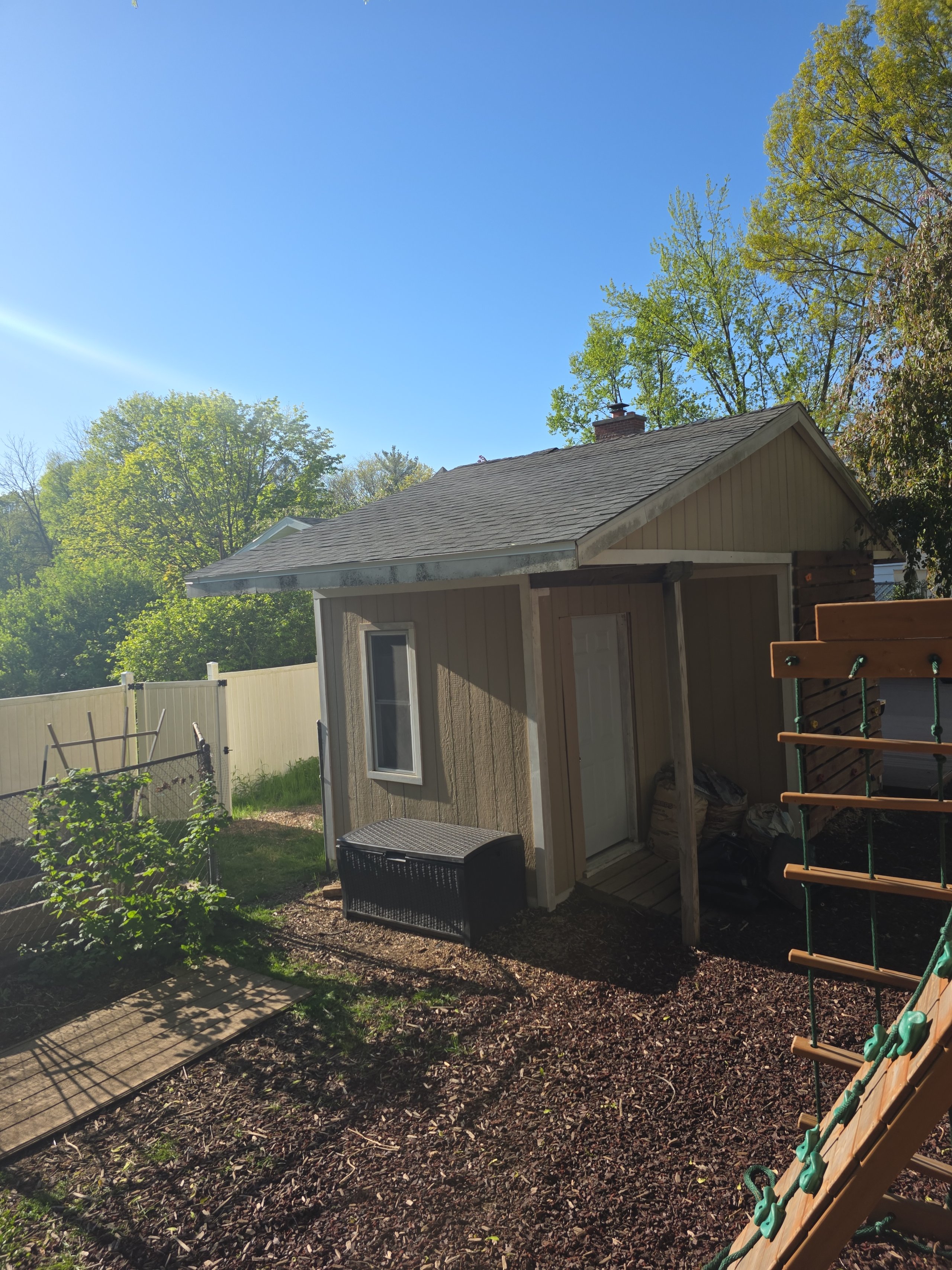 Small wooden shed in backyard with fence, trees, and mulched ground