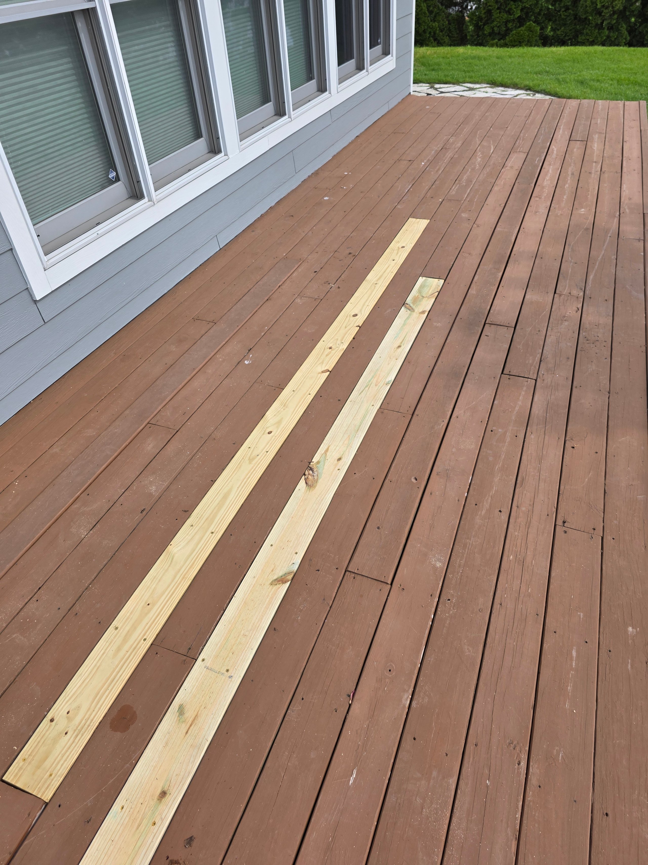 New wooden planks laid on brown deck next to house with windows
