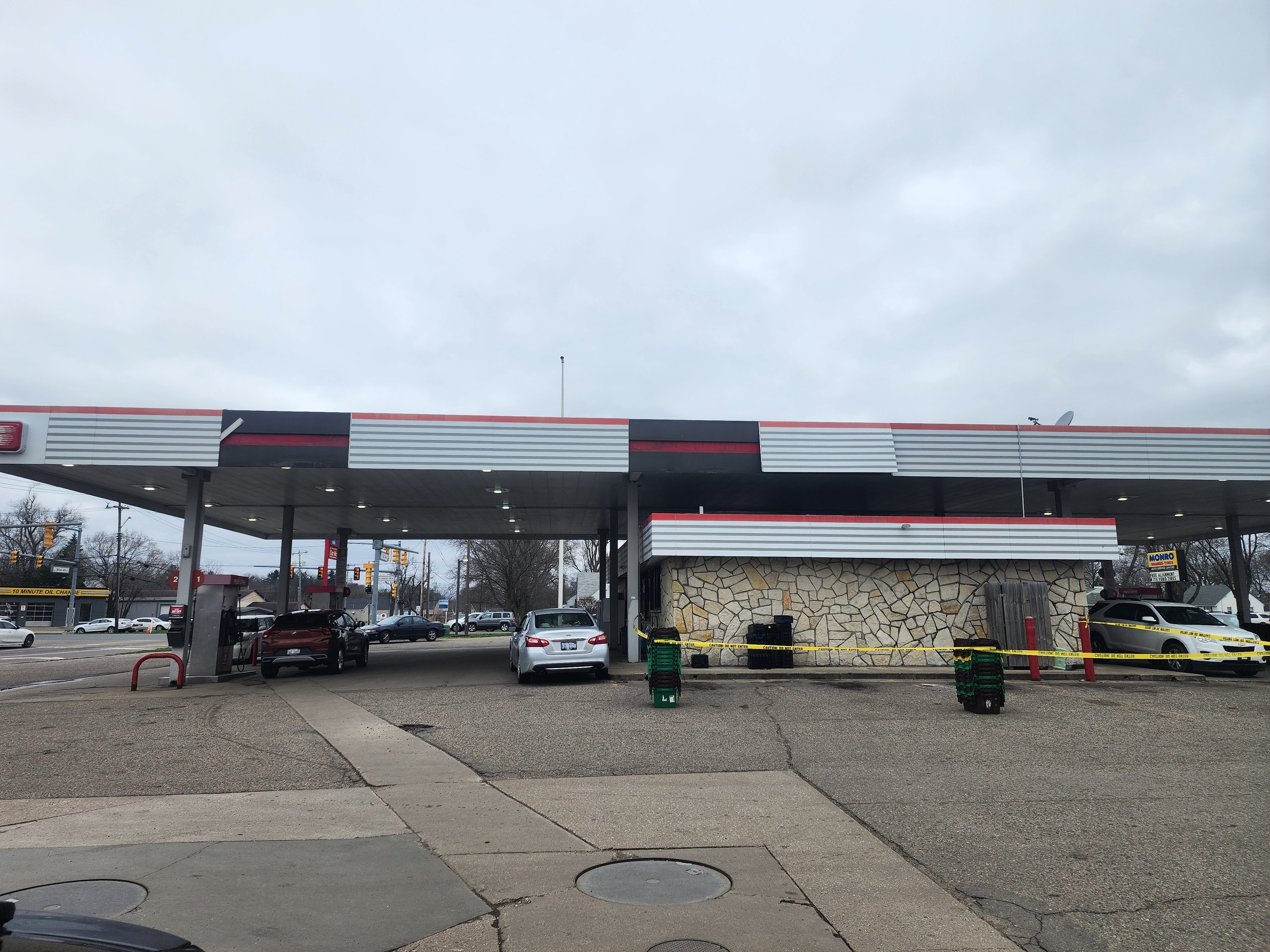 Gas station with cars parked under overcast sky, crime scene tape visible